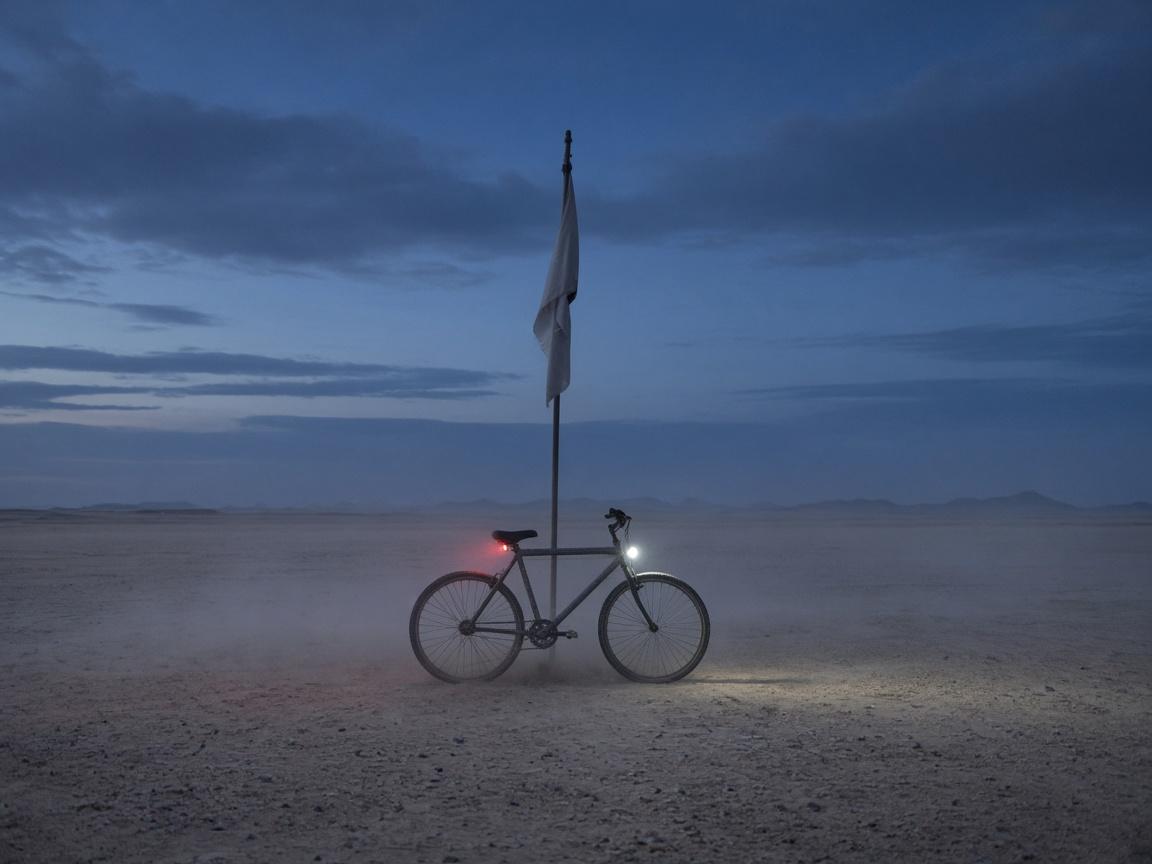 A dusty bicycle with a tall flag and lights on at dusk.